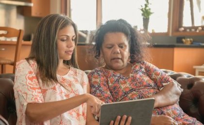 Two Indigenous women sitting down and looking at information on a digital device.
